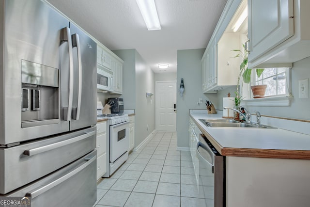 kitchen with light tile patterned flooring, a sink, stainless steel appliances, light countertops, and white cabinets