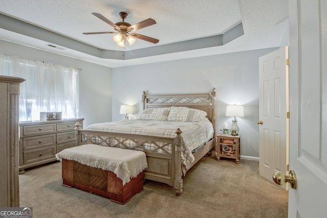 bedroom featuring a textured ceiling, a tray ceiling, visible vents, and light carpet