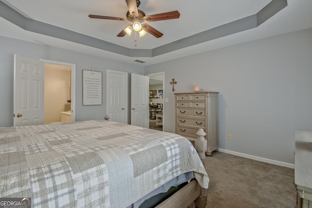 bedroom featuring ensuite bathroom, a tray ceiling, carpet, baseboards, and ceiling fan