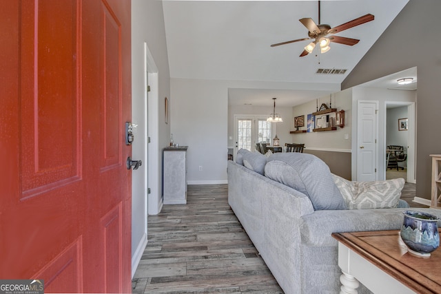 living room with visible vents, ceiling fan with notable chandelier, wood finished floors, baseboards, and vaulted ceiling