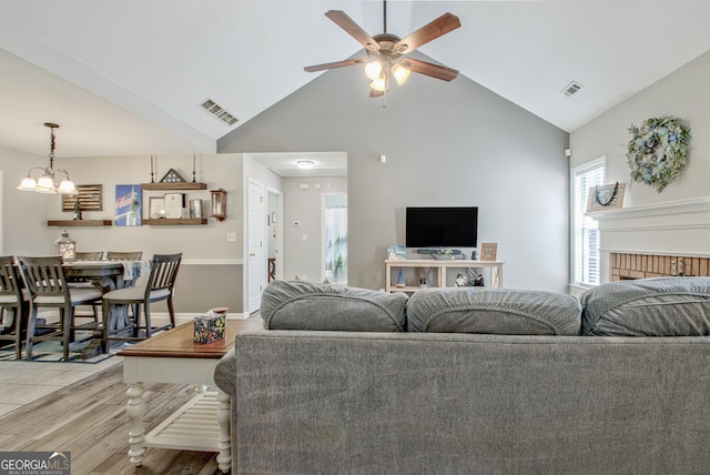 living room with light wood-type flooring, visible vents, high vaulted ceiling, and ceiling fan with notable chandelier