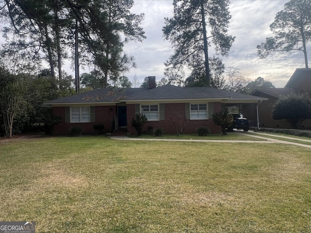 ranch-style house featuring brick siding, a front lawn, a chimney, a carport, and driveway