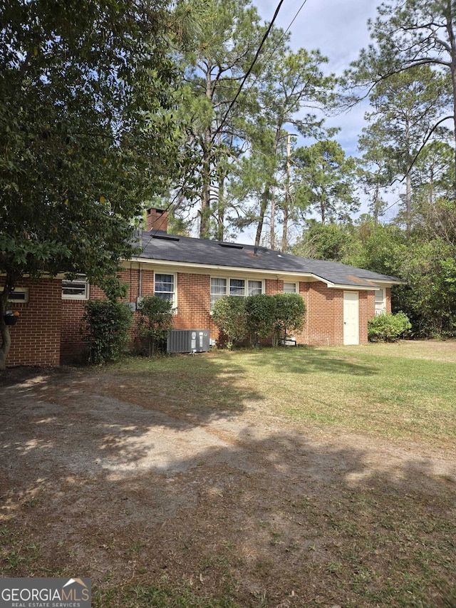 view of front facade with a front yard, solar panels, a chimney, central air condition unit, and brick siding