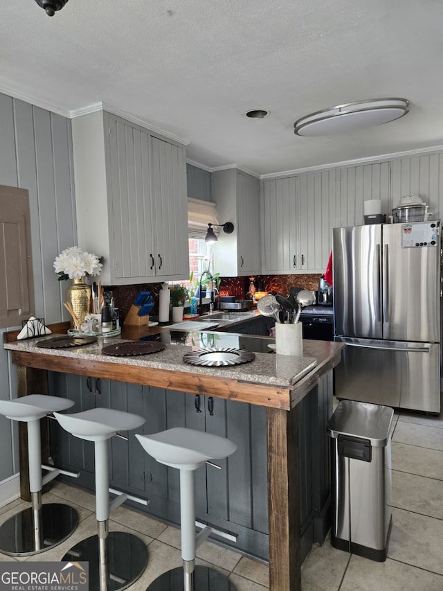 kitchen with a breakfast bar, decorative backsplash, a peninsula, freestanding refrigerator, and a sink