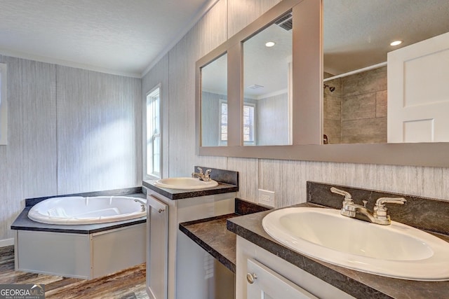 bathroom featuring crown molding, two vanities, a garden tub, and a sink