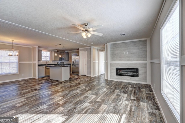 unfurnished living room featuring visible vents, ornamental molding, ceiling fan with notable chandelier, and dark wood-style flooring