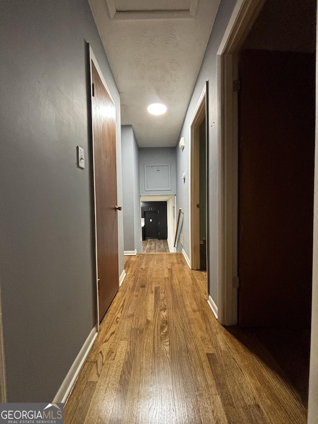 hallway with an upstairs landing, wood finished floors, and baseboards