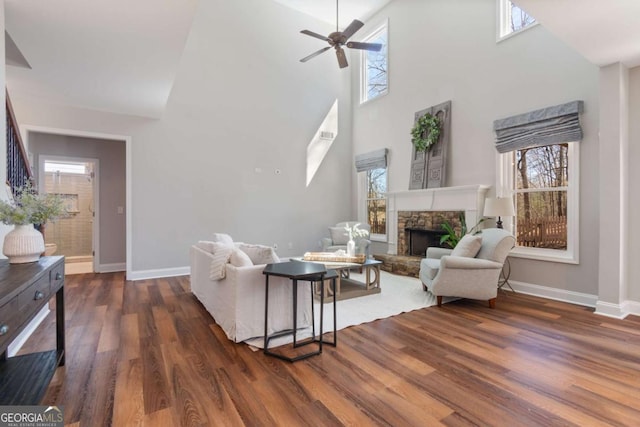 living area featuring a stone fireplace, baseboards, a ceiling fan, and wood finished floors