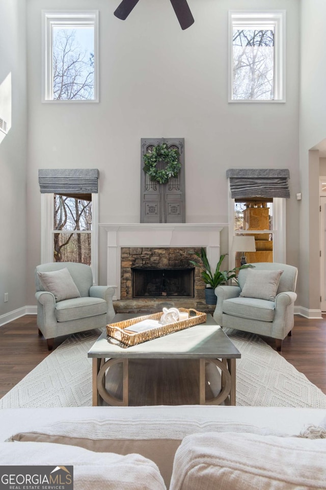 living area featuring a stone fireplace, wood finished floors, a towering ceiling, and a ceiling fan