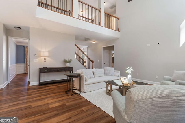 living room featuring a towering ceiling, baseboards, wood finished floors, and stairs