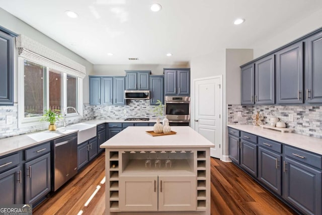 kitchen featuring open shelves, a center island, light countertops, appliances with stainless steel finishes, and a sink