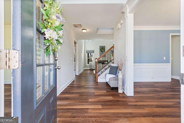 foyer entrance featuring a wainscoted wall, dark wood finished floors, stairs, and crown molding