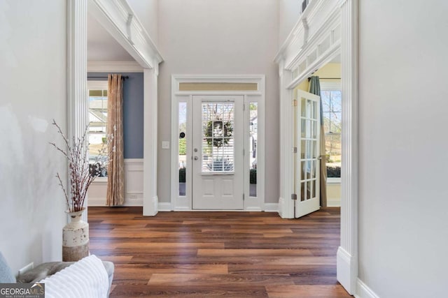 entryway with a towering ceiling, baseboards, wood finished floors, and crown molding