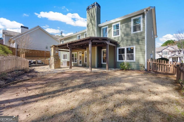 rear view of house featuring a patio area, a fenced backyard, and a chimney