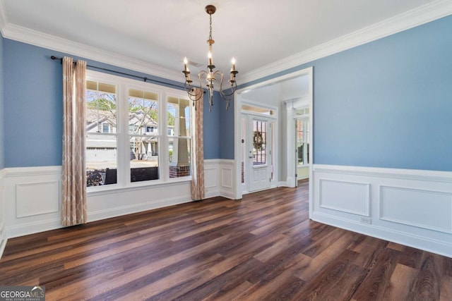 unfurnished dining area with a wainscoted wall, crown molding, dark wood-style flooring, and a chandelier