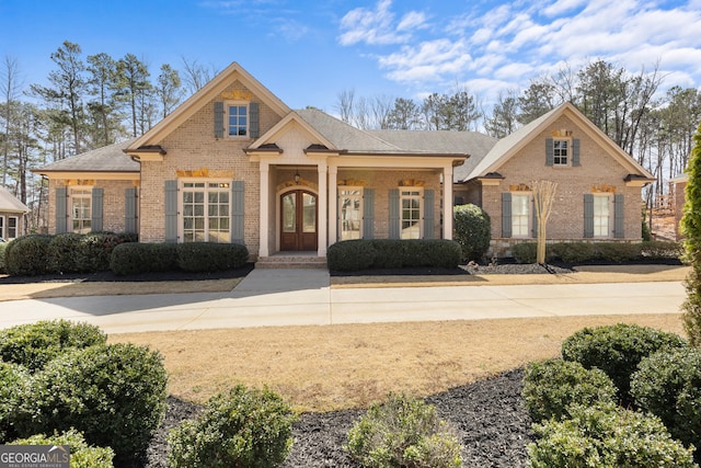 view of front of property featuring french doors, brick siding, and roof with shingles