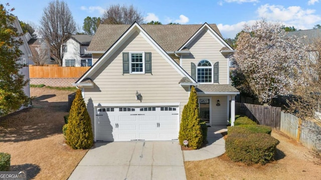 traditional-style house with driveway, a shingled roof, an attached garage, and fence