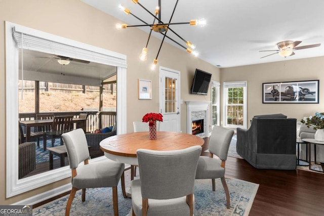 dining room with dark wood-style floors, ceiling fan with notable chandelier, and a fireplace