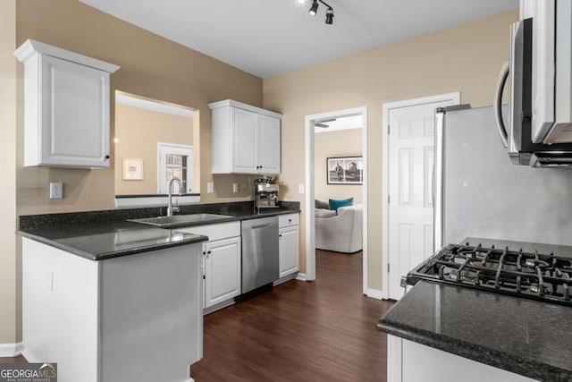 kitchen featuring dark wood finished floors, appliances with stainless steel finishes, a peninsula, white cabinetry, and a sink