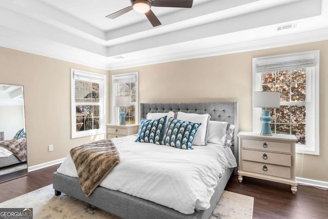 bedroom featuring visible vents, ceiling fan, baseboards, a tray ceiling, and wood finished floors