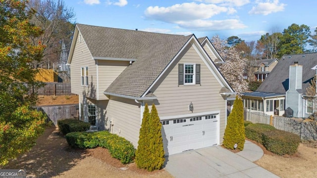 exterior space featuring a shingled roof, an attached garage, concrete driveway, and fence