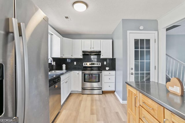 kitchen featuring dark countertops, under cabinet range hood, stainless steel appliances, white cabinetry, and a sink