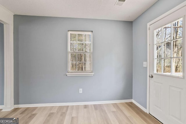 doorway to outside featuring a textured ceiling, baseboards, and light wood-style floors