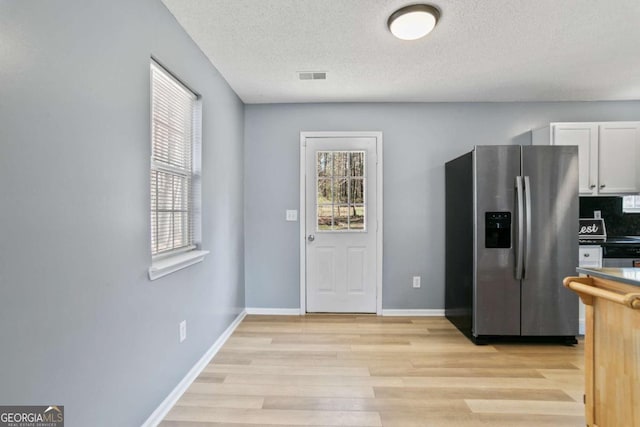 kitchen featuring visible vents, stainless steel refrigerator with ice dispenser, white cabinetry, light wood finished floors, and baseboards