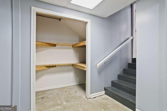 stairs with a paneled ceiling, baseboards, concrete floors, and a skylight