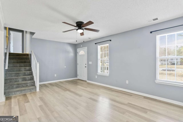 unfurnished living room featuring stairway, visible vents, baseboards, light wood-style floors, and a textured ceiling