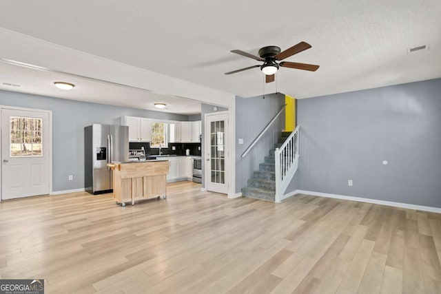 kitchen featuring a kitchen island, open floor plan, white cabinetry, appliances with stainless steel finishes, and light wood finished floors