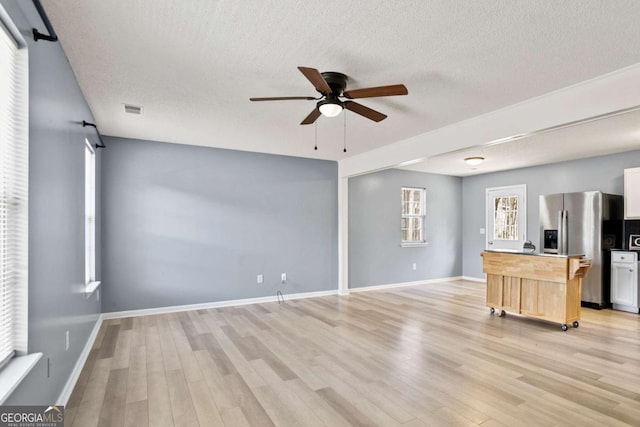 unfurnished living room with light wood-type flooring, a textured ceiling, visible vents, and a ceiling fan