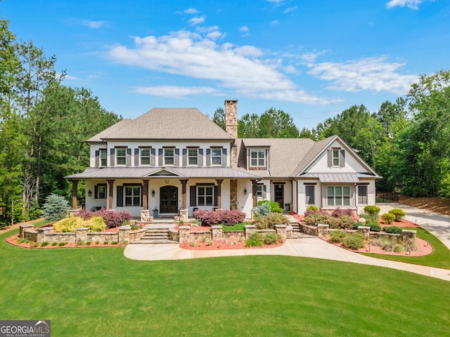 view of front of house with a standing seam roof, a porch, a chimney, a front lawn, and metal roof