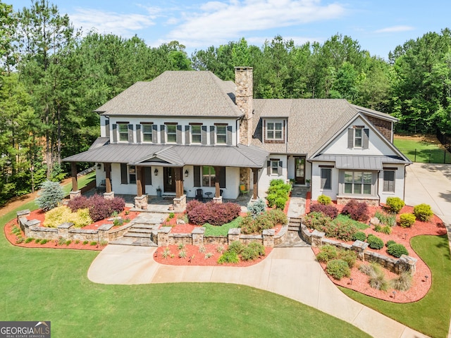 view of front of home featuring a front lawn, a standing seam roof, a porch, metal roof, and a chimney