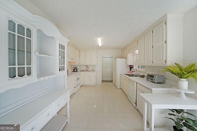 kitchen with a sink, white appliances, a textured ceiling, and light countertops