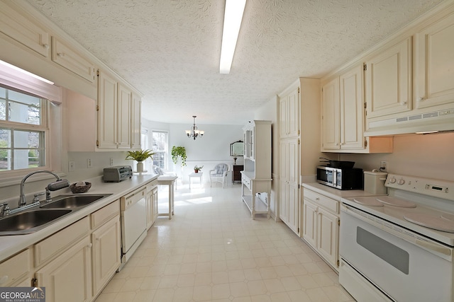 kitchen with a sink, under cabinet range hood, cream cabinets, white appliances, and a chandelier