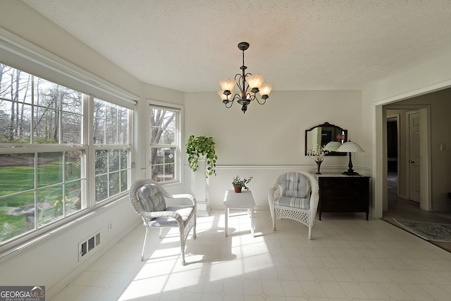 living area with visible vents, baseboards, a textured ceiling, and a chandelier