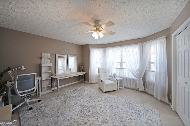 carpeted office space with baseboards, a textured ceiling, and a ceiling fan