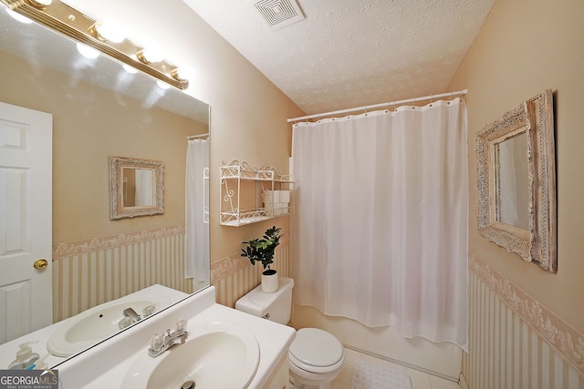 bathroom featuring visible vents, toilet, shower / tub combo with curtain, wainscoting, and a textured ceiling