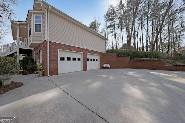 view of side of property with a garage, brick siding, driveway, and fence