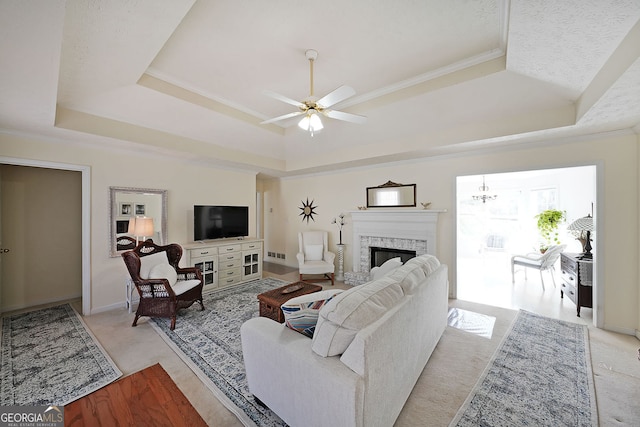 living area with a tray ceiling, a fireplace, crown molding, and ceiling fan with notable chandelier