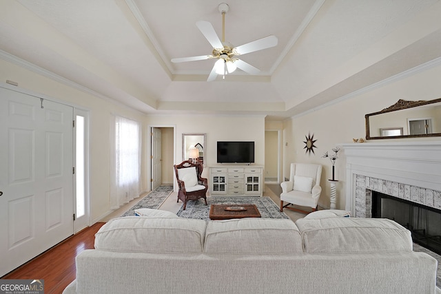 living room featuring a premium fireplace, ornamental molding, wood finished floors, a raised ceiling, and a ceiling fan