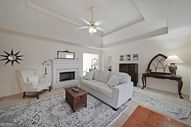 living area with a raised ceiling, a ceiling fan, and ornamental molding