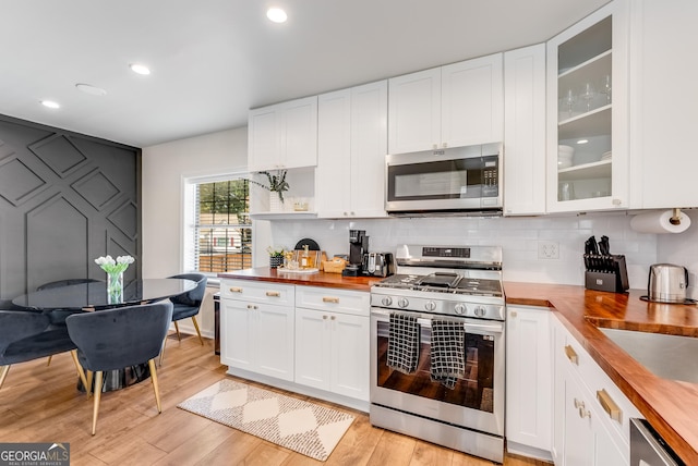 kitchen featuring backsplash, light wood-type flooring, appliances with stainless steel finishes, and butcher block counters