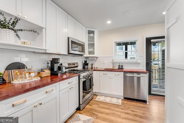 kitchen featuring light wood-style flooring, a sink, butcher block countertops, appliances with stainless steel finishes, and white cabinetry