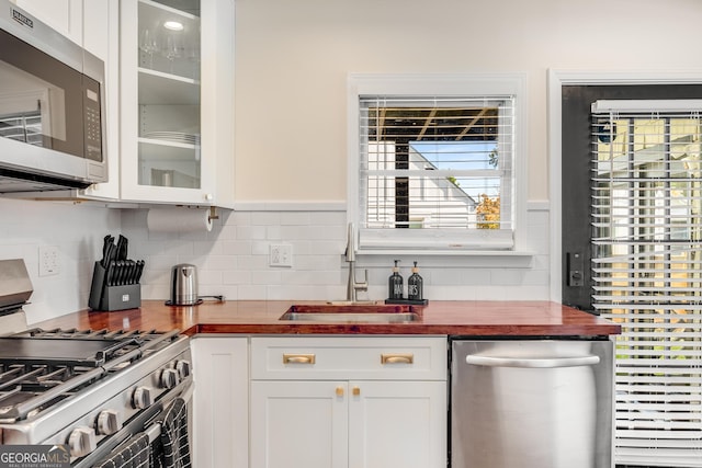 kitchen featuring a sink, stainless steel appliances, glass insert cabinets, white cabinetry, and tasteful backsplash