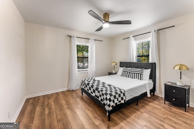 bedroom with multiple windows, a ceiling fan, baseboards, and wood-type flooring