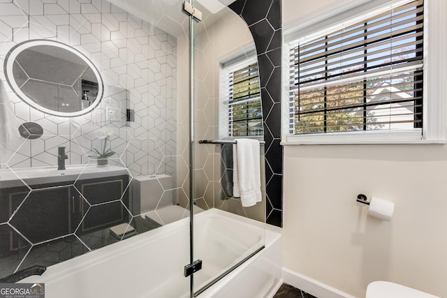 full bath with a sink, baseboards, and bath / shower combo with glass door