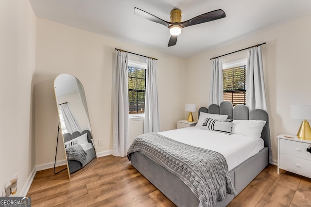 bedroom featuring a ceiling fan, multiple windows, wood finished floors, and baseboards