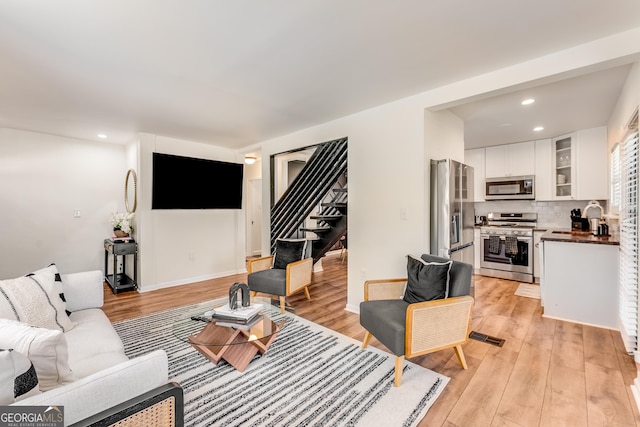 living area featuring recessed lighting, baseboards, stairs, and light wood finished floors